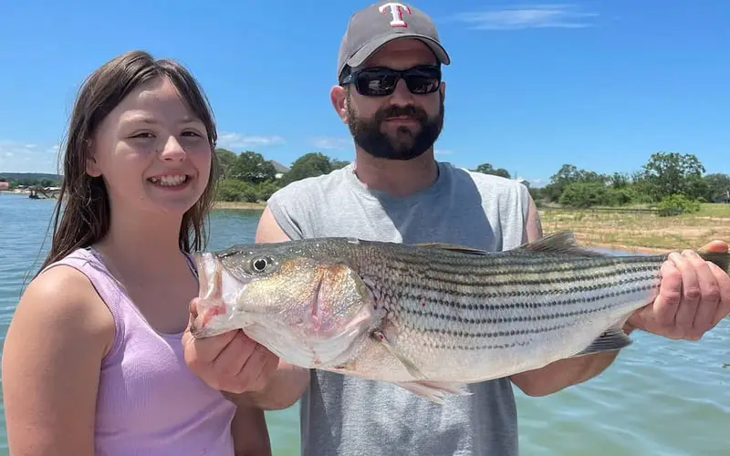 Two people holding a stripe bass fish