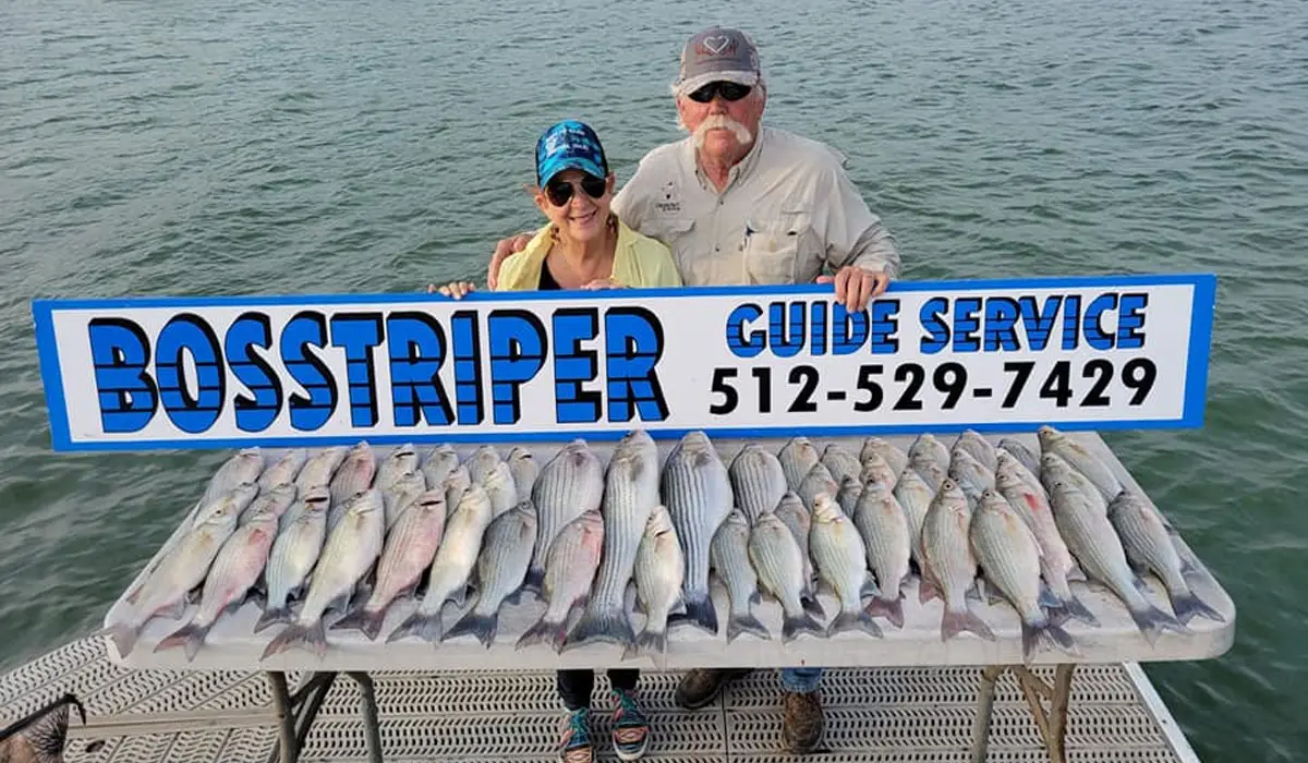 an elderly man and woman at Lake Buchanan holding signage of professional fishing guide
